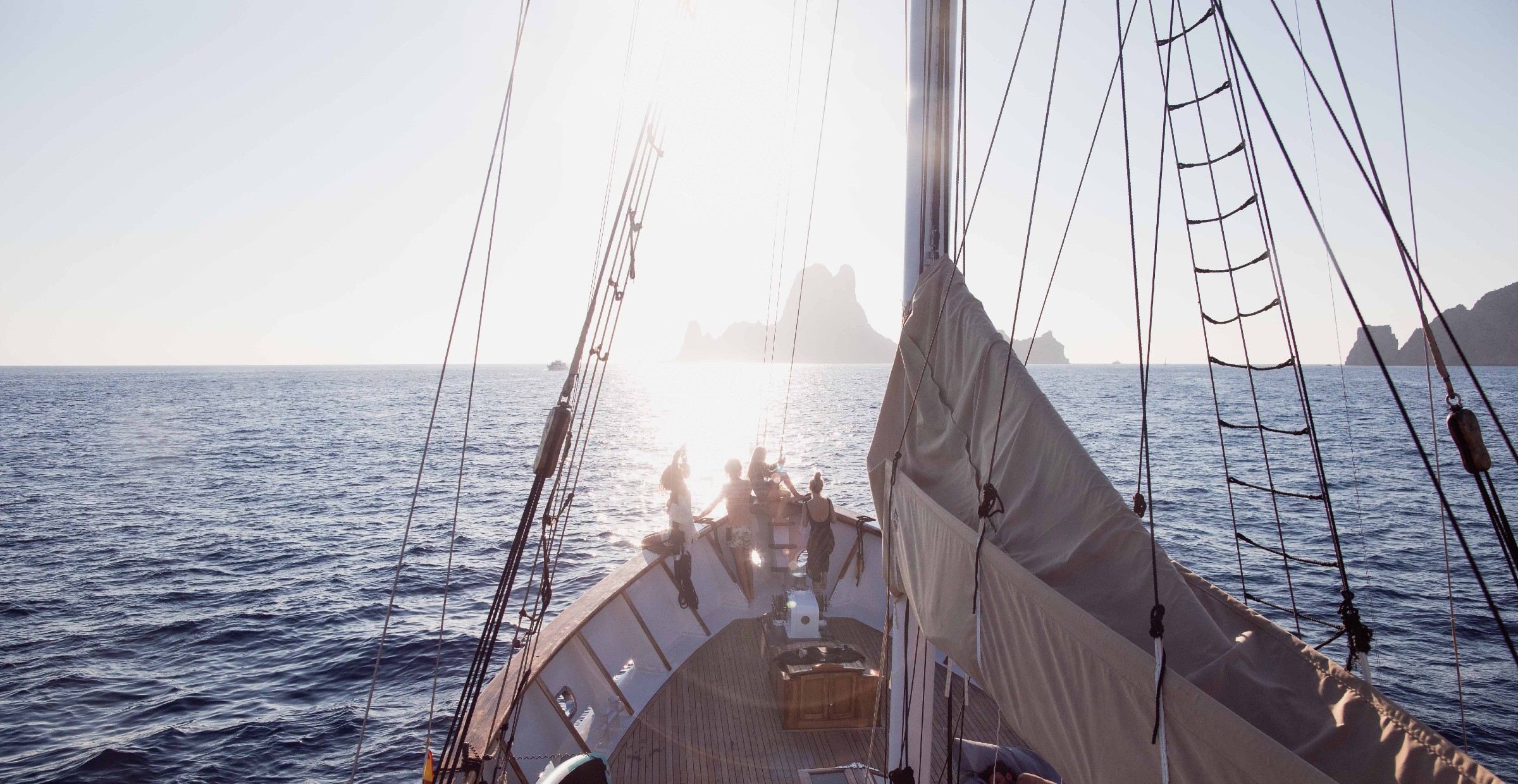 Boat heading towards sunset with rocks in horizon