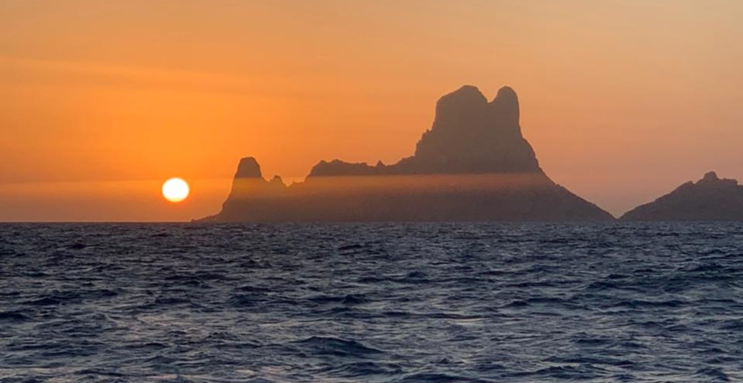 Sun setting over the sea with rocky island in the horizon